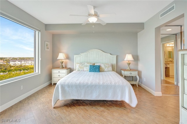 bedroom featuring light hardwood / wood-style floors, connected bathroom, multiple windows, and ceiling fan