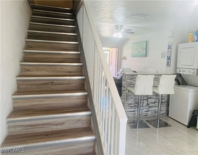 staircase with ceiling fan and stacked washer / dryer