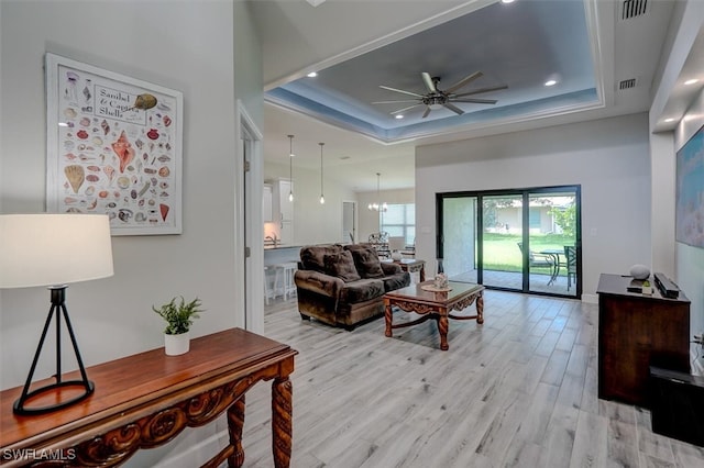 living room featuring ceiling fan with notable chandelier, light hardwood / wood-style floors, and a raised ceiling