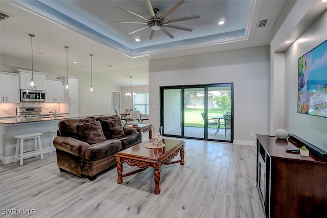 living room featuring ceiling fan with notable chandelier, light wood-type flooring, and a tray ceiling