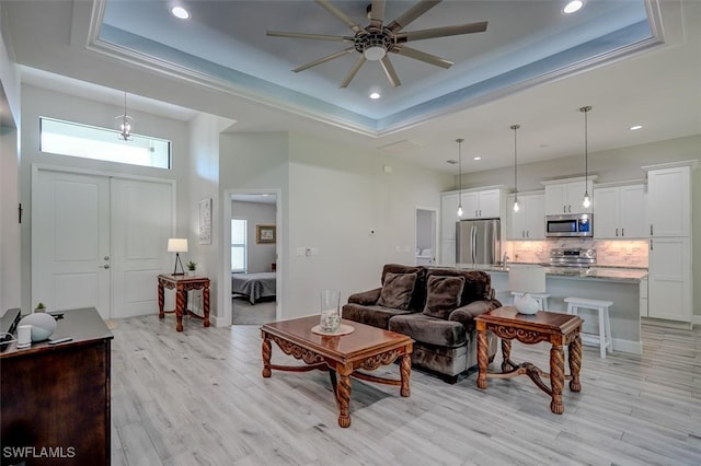 living room with light hardwood / wood-style flooring, a high ceiling, ceiling fan, and a raised ceiling