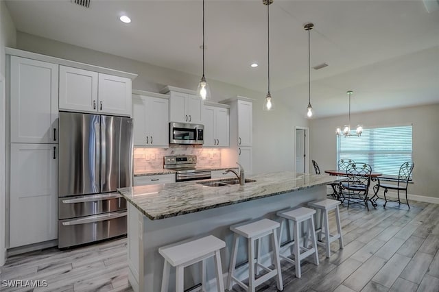 kitchen featuring sink, an island with sink, white cabinetry, stainless steel appliances, and light stone countertops