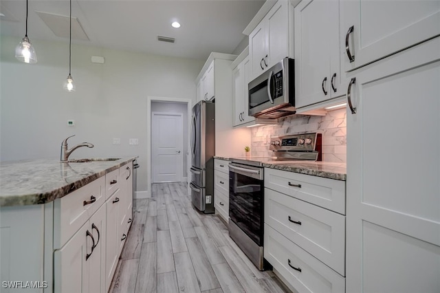 kitchen with light stone counters, white cabinets, hanging light fixtures, sink, and appliances with stainless steel finishes