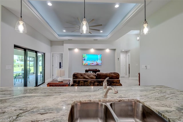 kitchen with hanging light fixtures, a raised ceiling, light stone countertops, ceiling fan, and sink