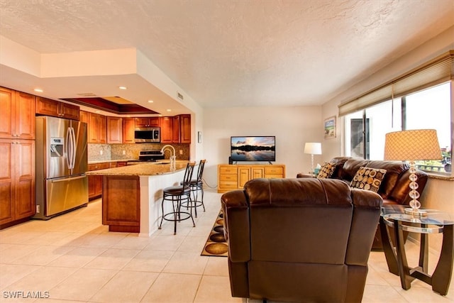 living room with light tile patterned flooring, a tray ceiling, sink, and a textured ceiling