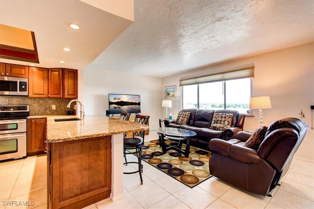 kitchen with sink, kitchen peninsula, a breakfast bar area, appliances with stainless steel finishes, and light tile patterned floors