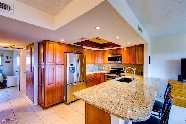 kitchen featuring light stone counters, sink, kitchen peninsula, stainless steel appliances, and a breakfast bar