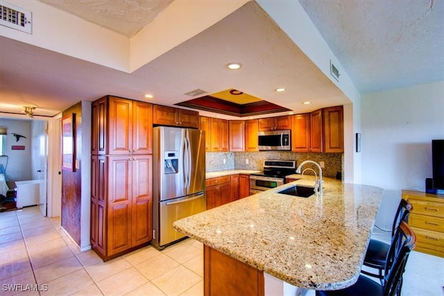 4906 Victoria Dr Unit 413, Cape Coral, FL 33904 - kitchen featuring stainless steel appliances, a peninsula, a sink, a raised ceiling, and light stone countertops