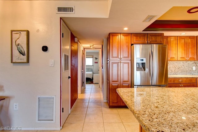 kitchen with light stone counters, stainless steel fridge, light tile patterned floors, and tasteful backsplash