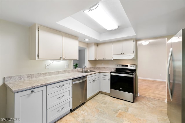 kitchen with a raised ceiling, stainless steel appliances, white cabinetry, and sink