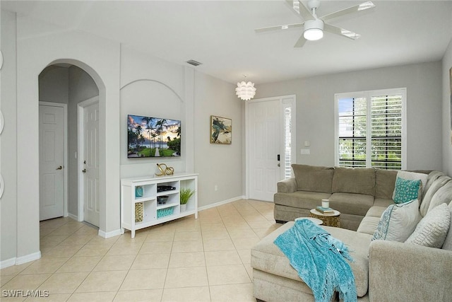 living room featuring a ceiling fan, light tile patterned floors, arched walkways, baseboards, and visible vents