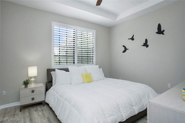 bedroom with wood finished floors, ceiling fan, and a raised ceiling
