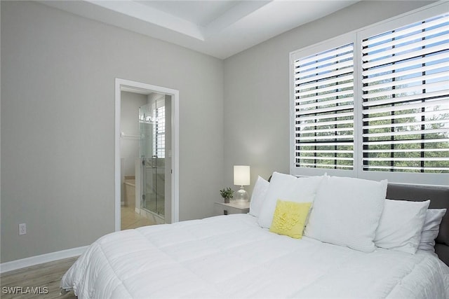 bedroom with ensuite bath, baseboards, multiple windows, and light wood-style flooring