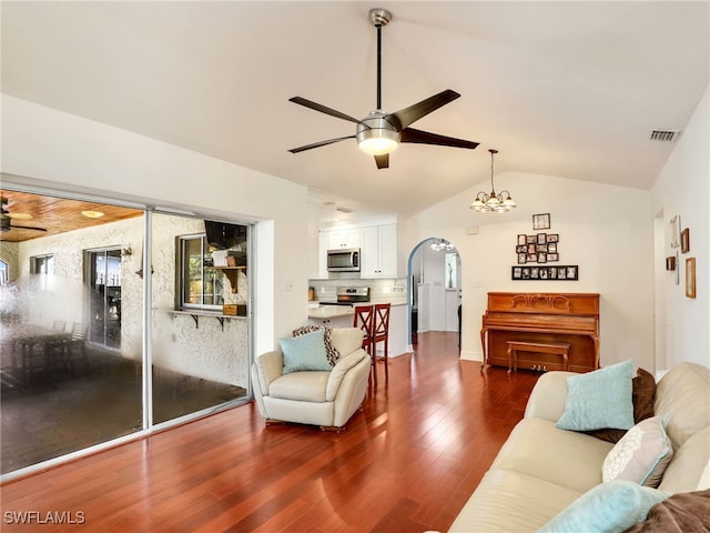 living room featuring ceiling fan with notable chandelier, vaulted ceiling, and dark wood-type flooring