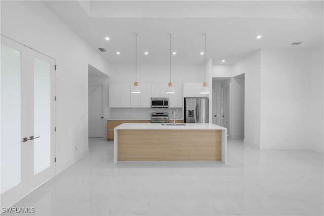 kitchen with hanging light fixtures, stainless steel appliances, a center island with sink, sink, and white cabinets