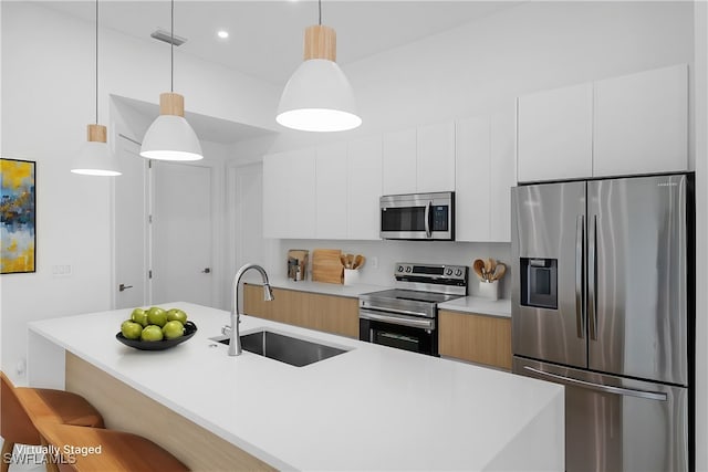 kitchen featuring white cabinetry, stainless steel appliances, sink, and hanging light fixtures