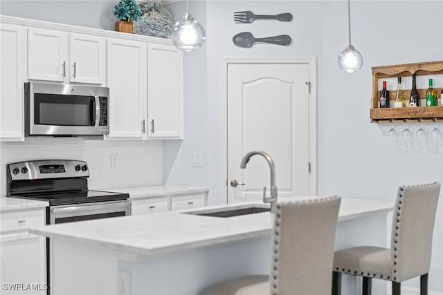 kitchen with white cabinets, sink, appliances with stainless steel finishes, decorative light fixtures, and a breakfast bar area