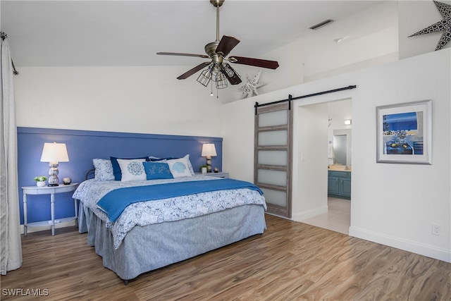 bedroom with lofted ceiling, hardwood / wood-style flooring, ensuite bath, a barn door, and ceiling fan