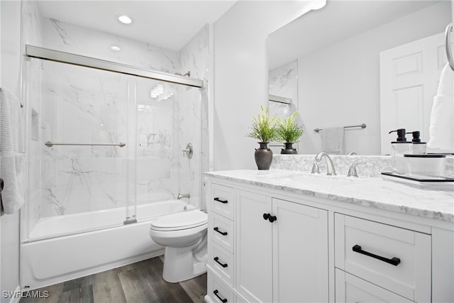 full bathroom with wood-type flooring, shower / bath combination with glass door, vanity, and toilet