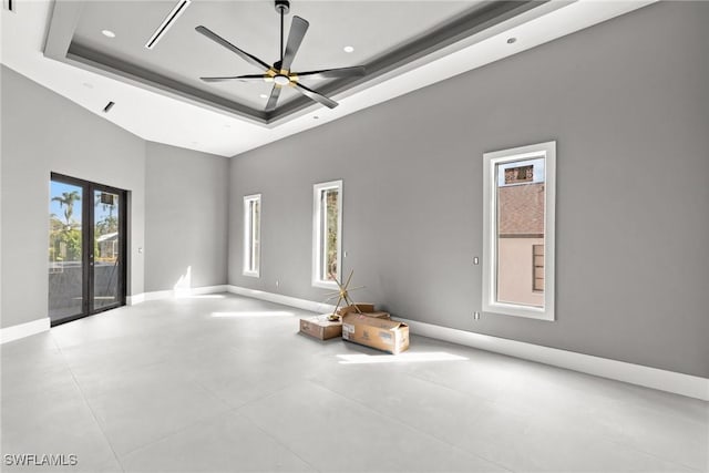 spare room featuring ceiling fan, a tray ceiling, a high ceiling, and baseboards