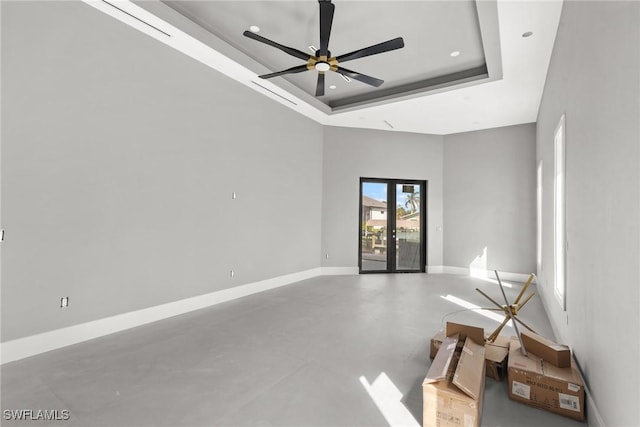 spare room with a towering ceiling, a ceiling fan, baseboards, french doors, and a raised ceiling