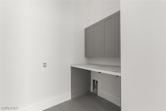 laundry room with cabinet space, dark tile patterned floors, and baseboards