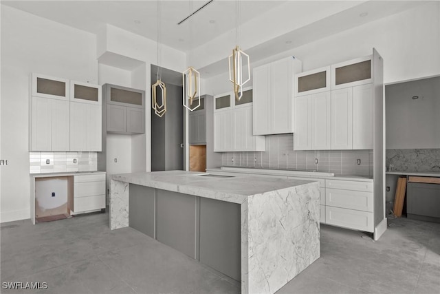 kitchen with light stone counters, a spacious island, backsplash, glass insert cabinets, and pendant lighting