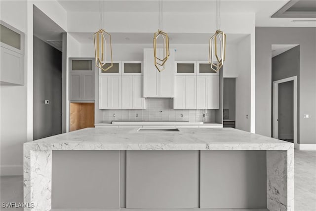 kitchen featuring white cabinets, decorative backsplash, a large island, light stone counters, and glass insert cabinets