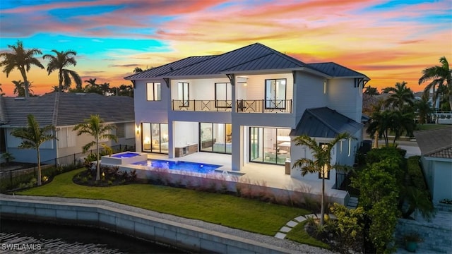 back house at dusk with a swimming pool with hot tub, a yard, a balcony, and a patio