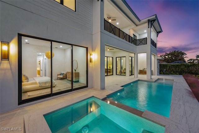 pool at dusk featuring a patio area and an in ground hot tub