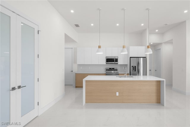 kitchen featuring white cabinets, appliances with stainless steel finishes, a kitchen island with sink, pendant lighting, and sink