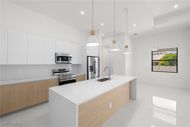 kitchen with sink, stainless steel appliances, decorative light fixtures, white cabinets, and a kitchen island with sink