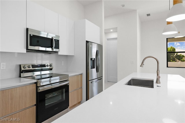 kitchen featuring white cabinetry, appliances with stainless steel finishes, decorative light fixtures, and sink