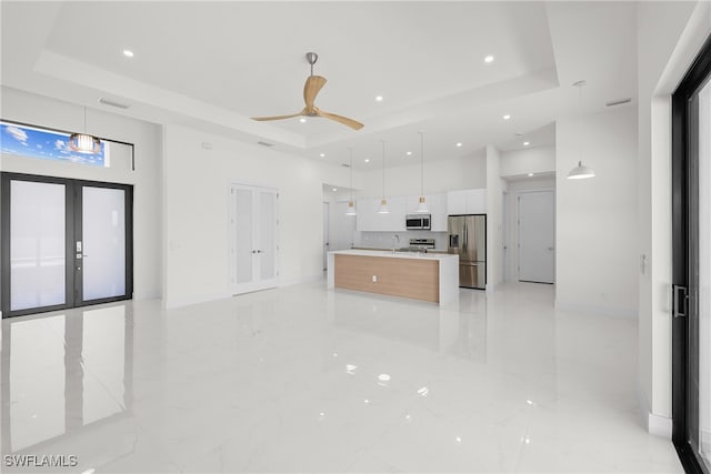 kitchen with a raised ceiling, a spacious island, appliances with stainless steel finishes, white cabinetry, and decorative light fixtures