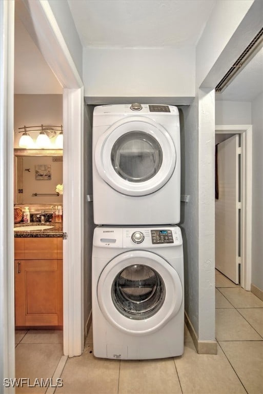 clothes washing area featuring sink, light tile patterned floors, and stacked washing maching and dryer