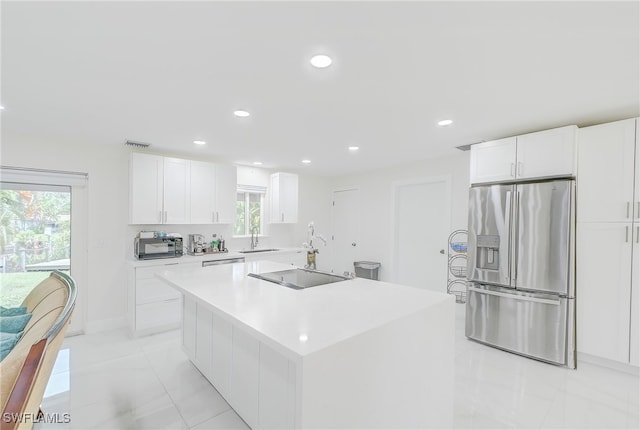 kitchen featuring white cabinets, an island with sink, stainless steel fridge, sink, and black electric stovetop