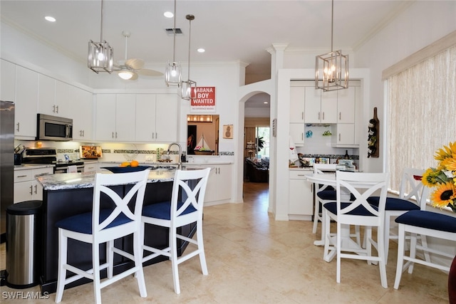 kitchen featuring decorative light fixtures, white cabinetry, a kitchen island with sink, and appliances with stainless steel finishes