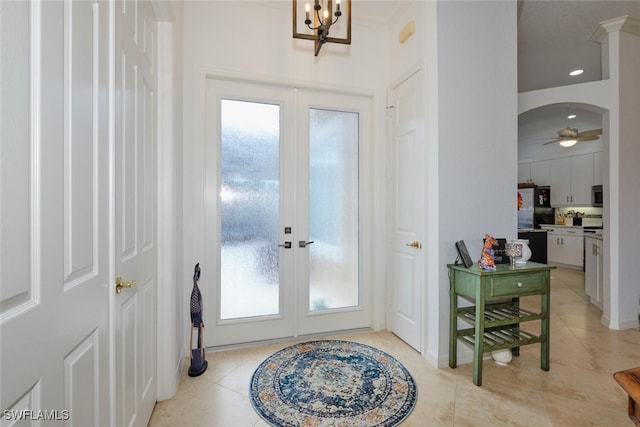 foyer entrance with ceiling fan with notable chandelier, a healthy amount of sunlight, light tile patterned floors, and french doors