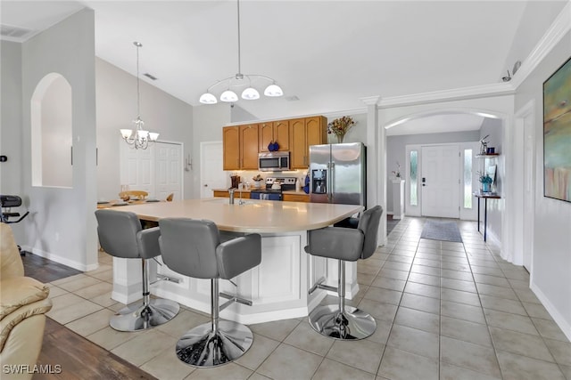 kitchen featuring high vaulted ceiling, stainless steel appliances, decorative light fixtures, and crown molding