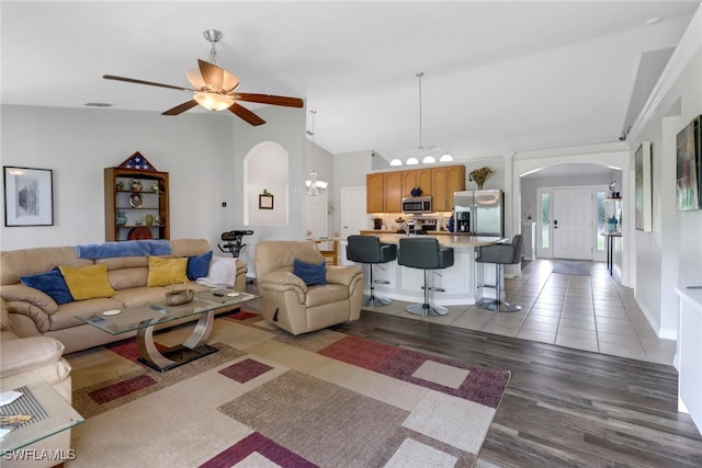 living room featuring ceiling fan with notable chandelier, vaulted ceiling, and light hardwood / wood-style floors