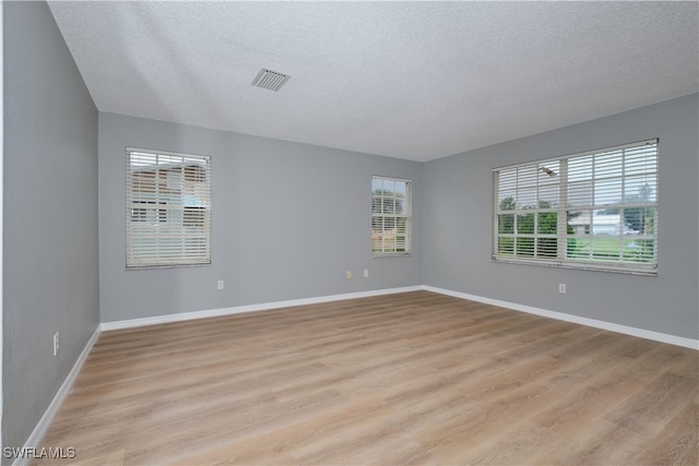 spare room featuring light wood finished floors, baseboards, visible vents, and a textured ceiling