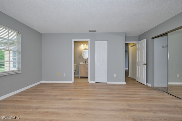 unfurnished bedroom with light wood-style flooring, visible vents, a textured ceiling, and two closets
