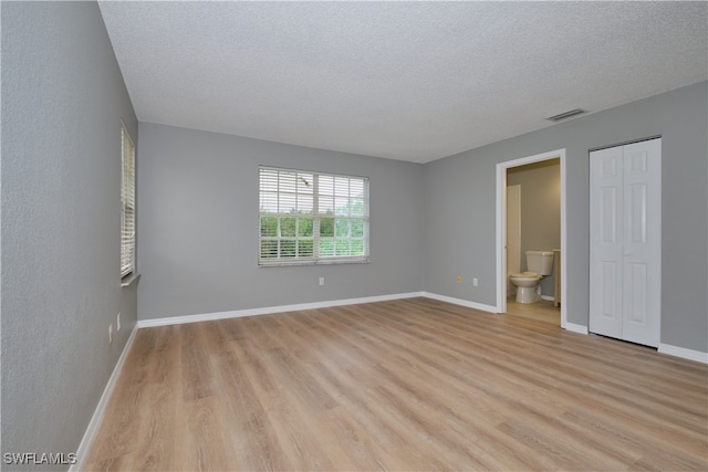 unfurnished bedroom featuring ensuite bathroom, a textured ceiling, light wood-type flooring, baseboards, and visible vents