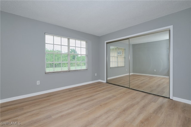 unfurnished bedroom featuring light wood finished floors, baseboards, a textured ceiling, and a closet