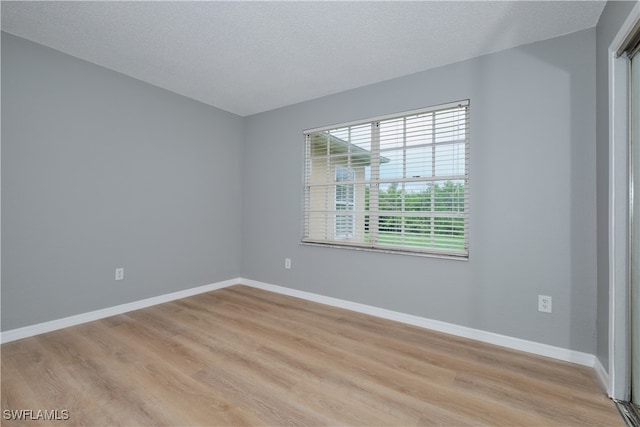 empty room featuring light wood-style flooring, a textured ceiling, and baseboards