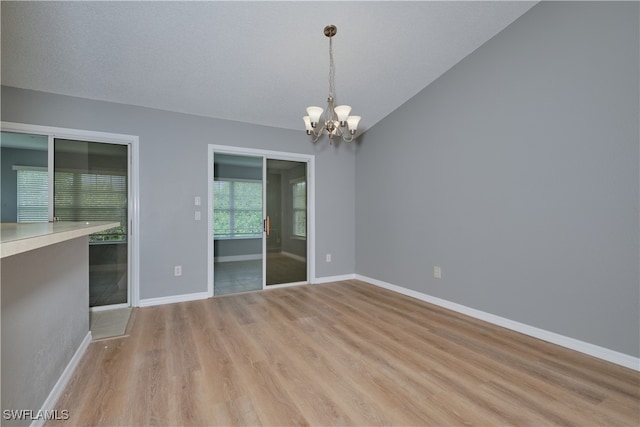 unfurnished room with lofted ceiling, light wood finished floors, baseboards, and a notable chandelier