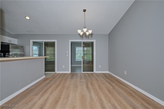 interior space featuring a textured ceiling, light wood-type flooring, an inviting chandelier, and a healthy amount of sunlight