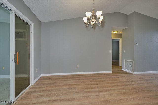 empty room featuring light hardwood / wood-style flooring, vaulted ceiling, a textured ceiling, a notable chandelier, and a wall unit AC