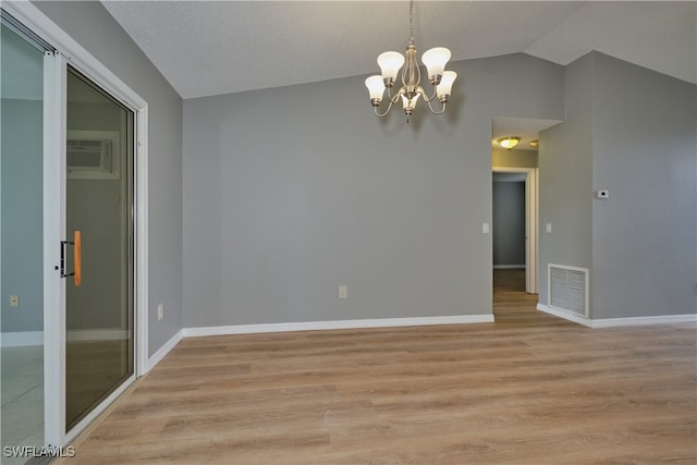 spare room with light wood finished floors, vaulted ceiling, visible vents, an inviting chandelier, and a wall mounted AC