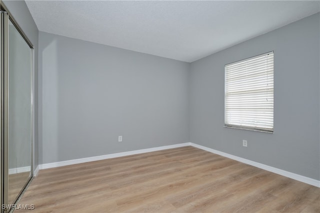 unfurnished bedroom featuring light wood finished floors, baseboards, and a closet